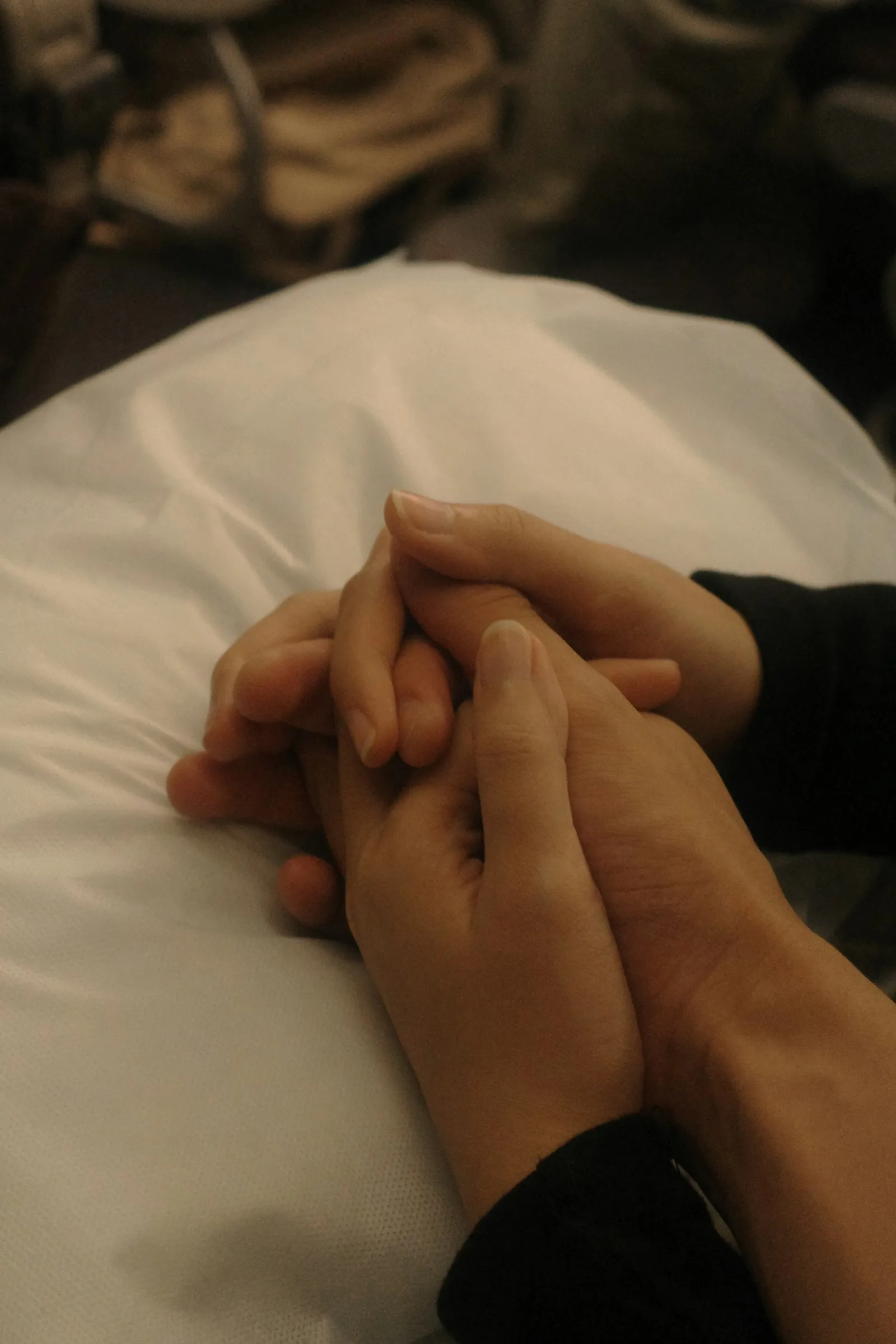 Two hands gently holding each other on a pillow