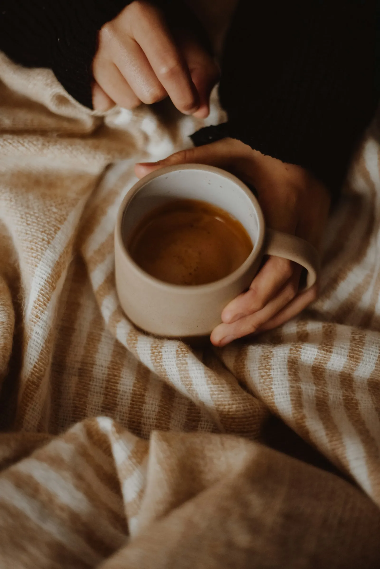 Hands wrapped around a warm mug on a soft blanket